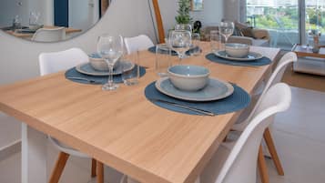 A dining table set with plates, bowls, and wine glasses, surrounded by white chairs.