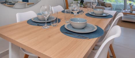 A dining table set with plates, bowls, and wine glasses, surrounded by white chairs.