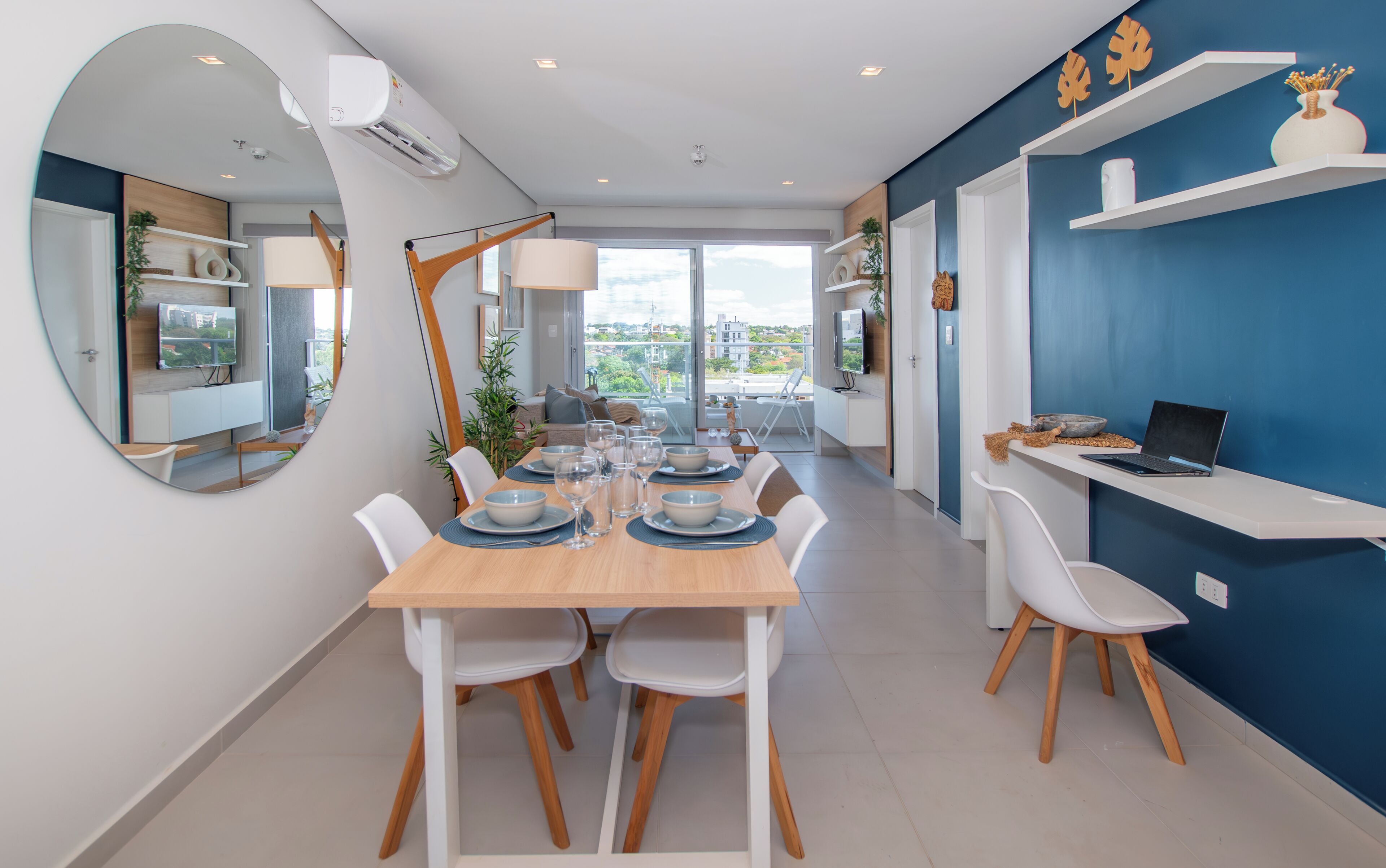 A modern dining area with a wooden table set for four, white chairs, and a large window offering a view of the city.