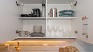 A kitchen with white cabinets, a coffee maker, a kettle, and a set of plates and glasses. - Corporate Stays First Living - 806 (Asunción)