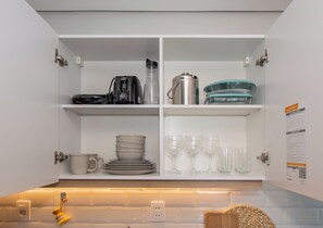 A kitchen with white cabinets, a coffee maker, a kettle, and a set of plates and glasses. - Corporate Stays First Living - 806 (Asunción)