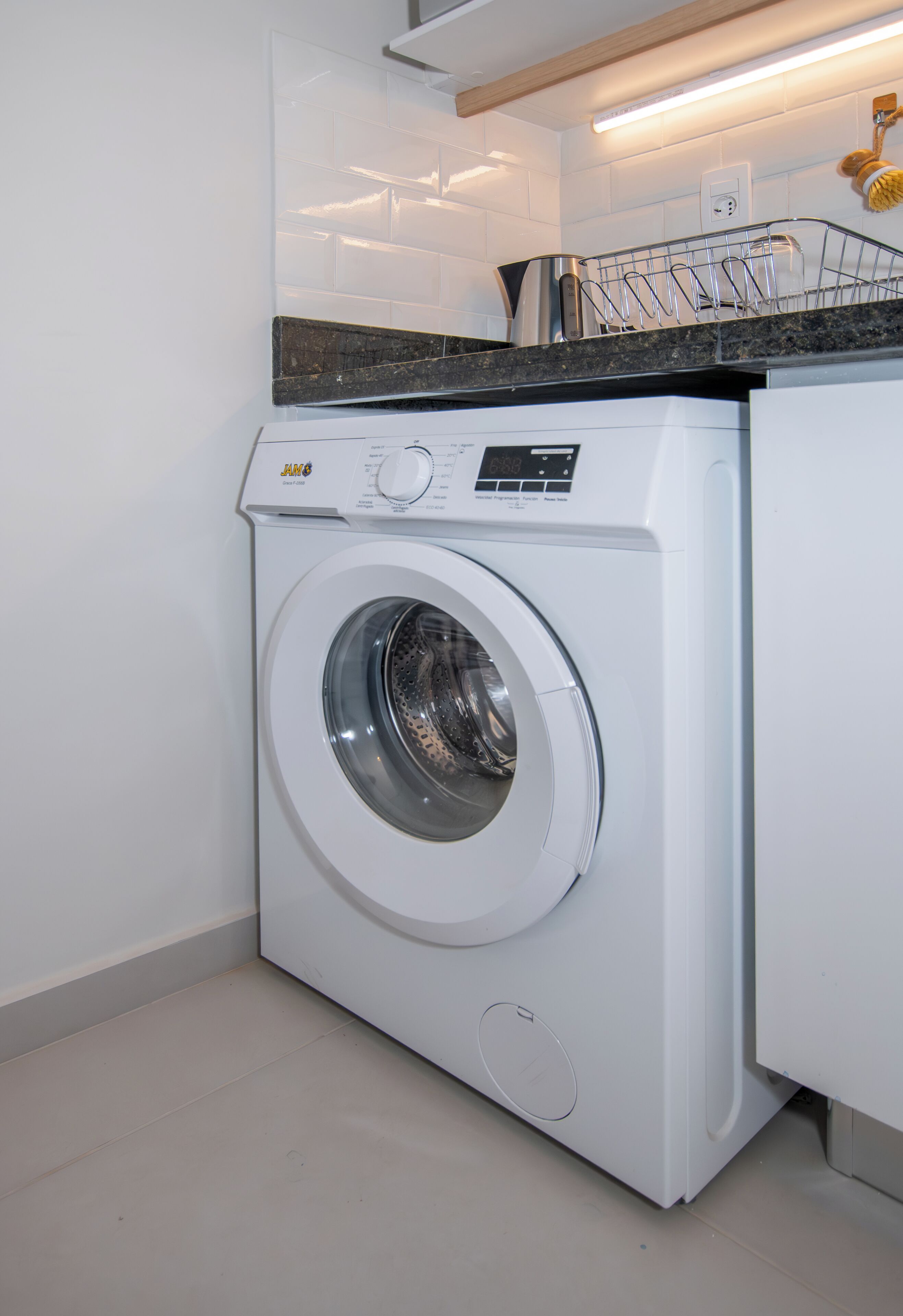 Eine moderne, kompakte Waschmaschine in einem sauberen Waschraum mit weißen Wänden und einer Arbeitsplatte darüber.