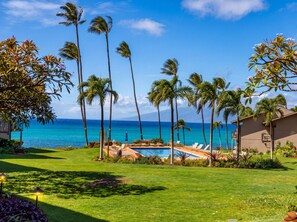 A pool area with lounge chairs, palm trees, and a view of the ocean. - Mahina Surf Oceanfront Condo | Ground Floor | A/C (Lahaina)