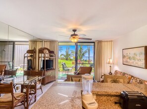 A hotel room with a dining area, a television, a blender, a toaster, and a view of a tropical landscape. - Mahina Surf Oceanfront Condo | Ground Floor | A/C (Lahaina)