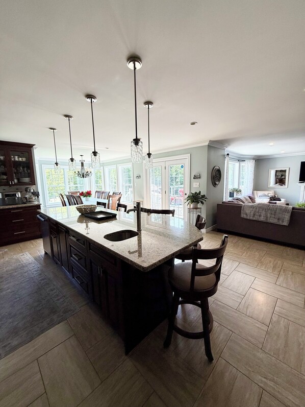 A spacious kitchen with a large island, pendant lighting, and a view of the outdoors through large windows.