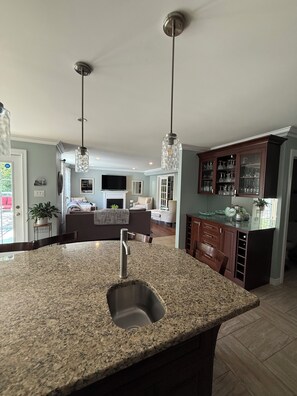 A kitchen with granite countertops, a stainless steel sink, pendant lighting, and a dining area with a table and chairs.