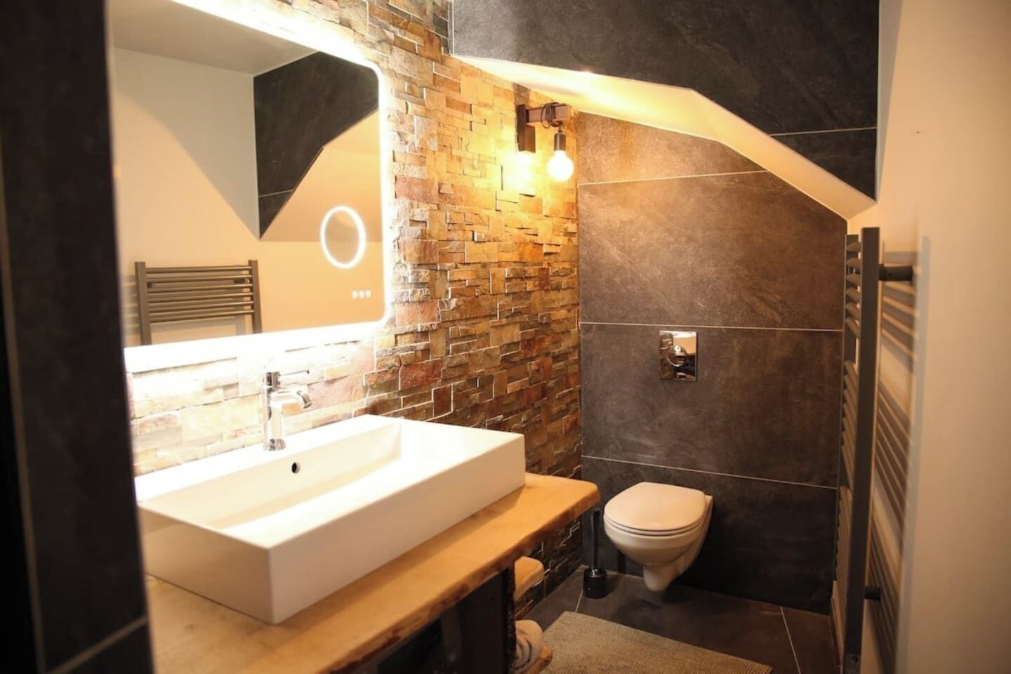 A modern bathroom with a stone wall, a white sink, and a toilet.