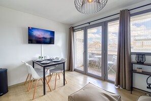 A modern dining area with a flat-screen TV, a dining table set for two, and a sliding glass door leading to an outdoor balcony. - Le Studio des Peupliers - 30m de la plage (Bray-Dunes)