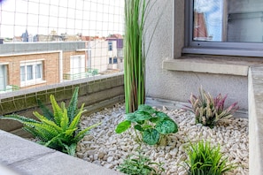 A balcony with a view of buildings, a concrete ledge, and various plants. - Le Studio des Peupliers - 30m de la plage (Bray-Dunes)
