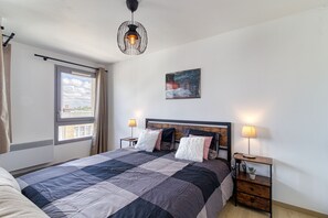 Ein Schlafzimmer mit einem großen Bett, zwei Nachttischlampen, einem Bild an der Wand und einem Fenster mit Vorhängen.