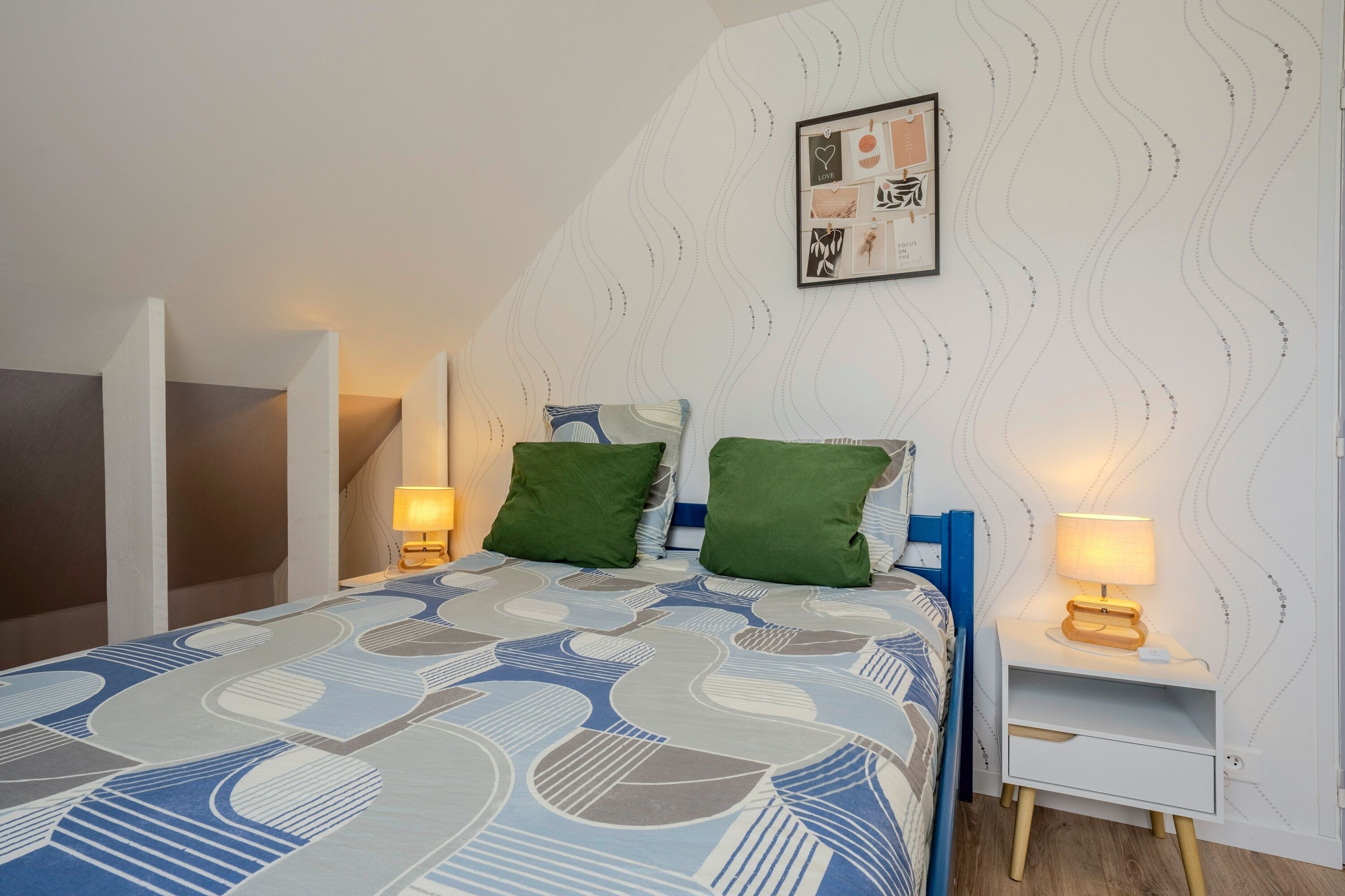 Une chambre à coucher avec un lit, deux lampes de chevet, un tableau encadré au mur et une couvre-lit à motifs.