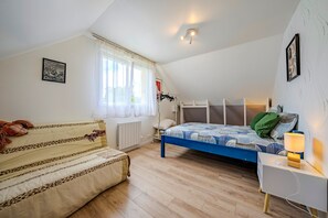 Ein Schlafzimmer mit Bett, Sofa, einem Fenster mit Vorhängen, Heizkörper und Wandleuchte.