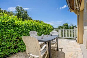 Eine Terrasse im Freien mit Tisch und Stühlen, umgeben von einem Hecken und einem weißen Zaun.