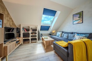Ein Loft-Wohnraum mit schrägem Dach, einer eingebauten Bücherwand, einem Sofa und einem Esstisch.