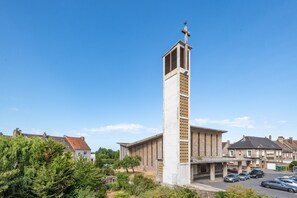 Eine hohe, weiße Kirche mit Kruzifix, umgeben von Wohnhäusern und parkenden Autos.