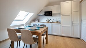 A modern kitchen with white cabinetry, a microwave, and a dining area with a wooden table and chairs. - Vigie d'Opale - Nausicaá & plage à 700 m (Boulogne-Sur-Mer)
