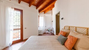 Un dormitorio con una cama grande, vigas de madera en el techo, una puerta a un balcón y una pequeña mesa con una silla.