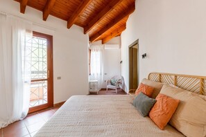 Ein Schlafzimmer mit einem großen Bett, Holzbalkendecke, einer Balkontür und einem kleinen Tisch mit Stuhl.