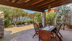Un patio al aire libre con una mesa y sillas de madera, rodeado de macetas con plantas y un muro de piedra.