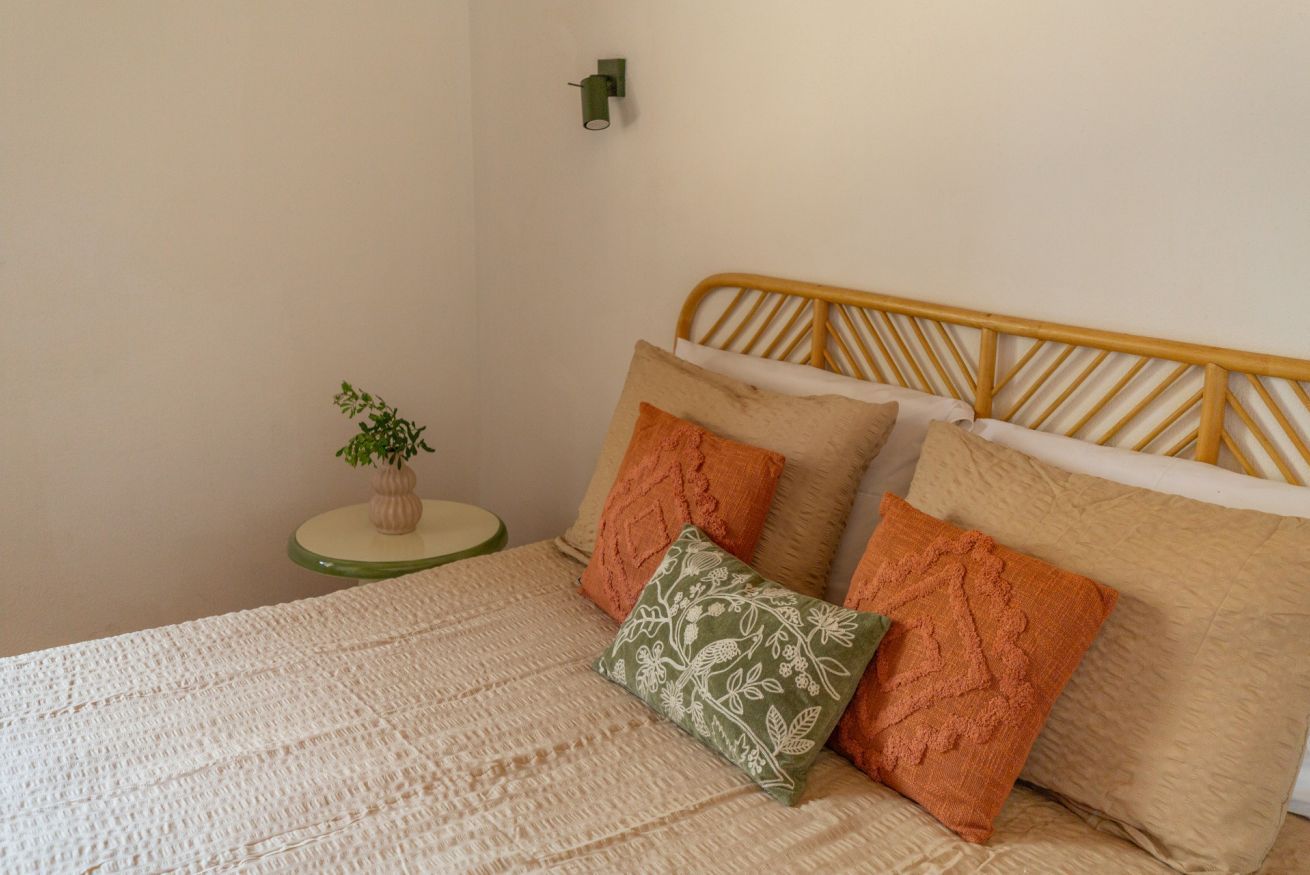 Una cama con cabecera de madera, una mesita de noche verde con una planta y una lámpara fijada a la pared.