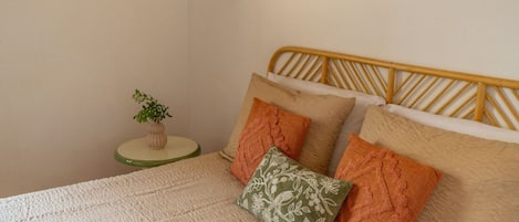 Una cama con cabecera de madera, una mesita de noche verde con una planta y una lámpara fijada a la pared.