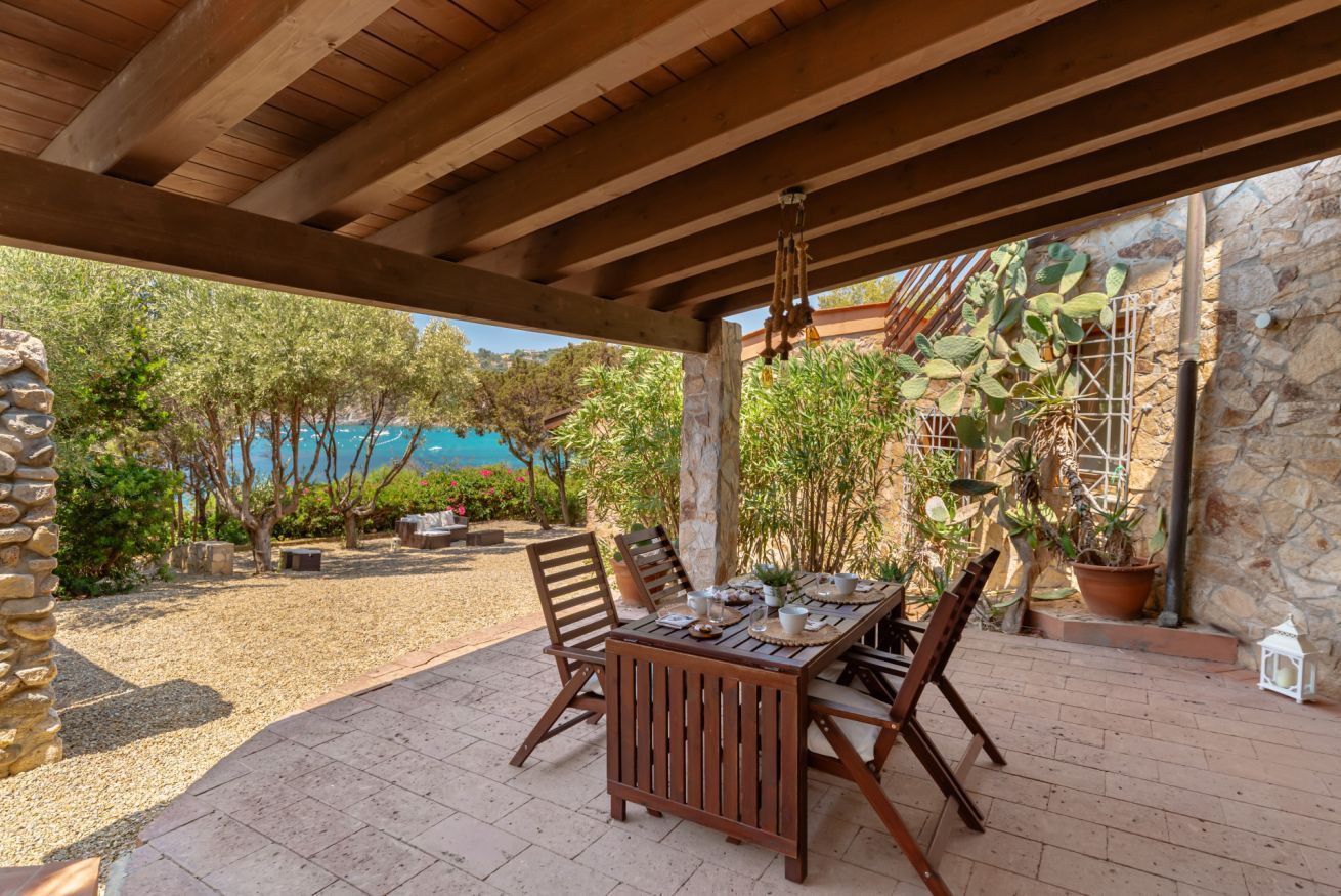 An outdoor patio with a wooden table and chairs, surrounded by stone walls and potted plants.