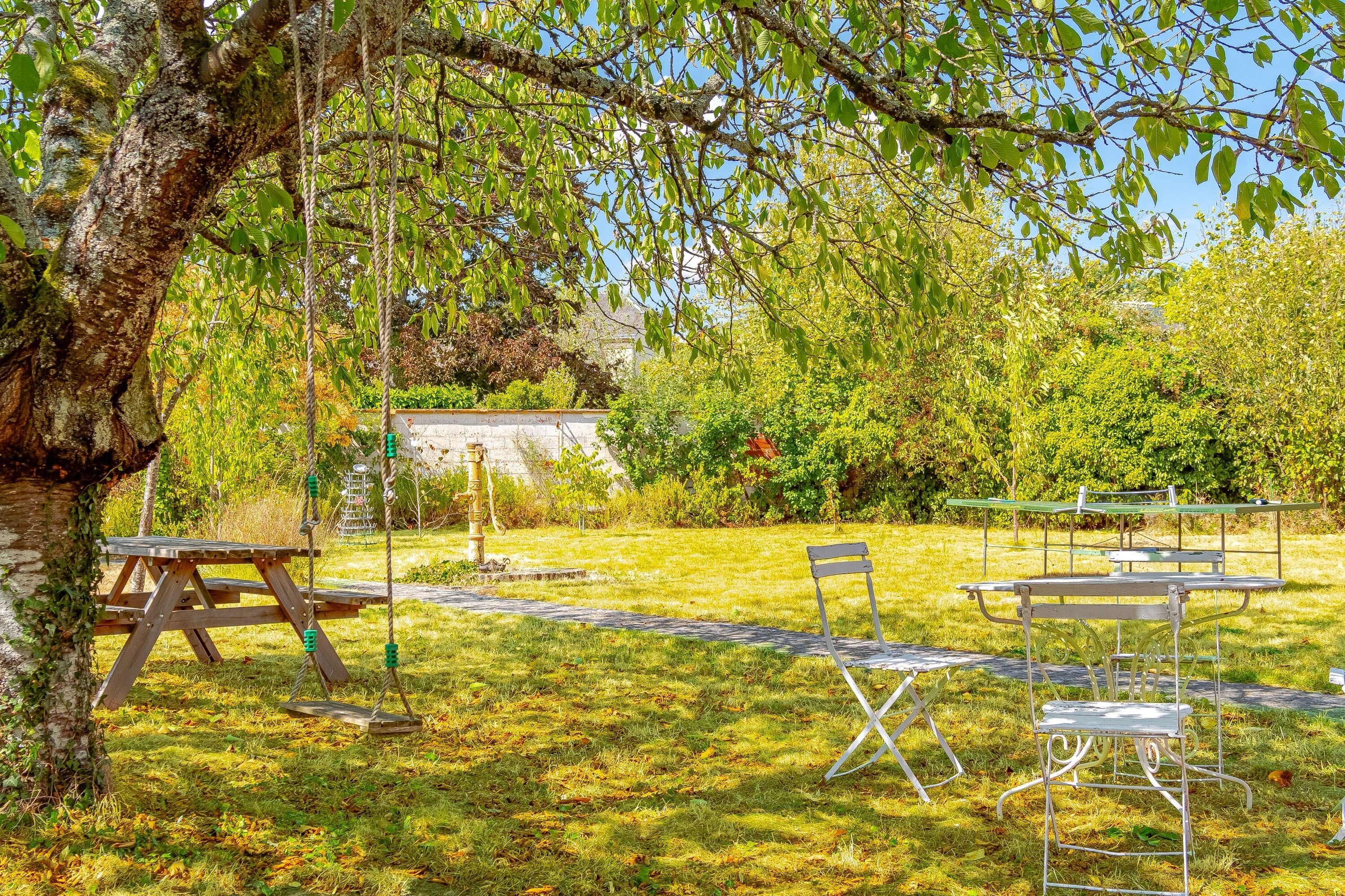 Un espace extérieur aménagé avec des tables de pique-nique et des chaises, entouré d’arbres et d’herbe.