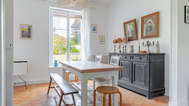 Un coin repas avec une table et des bancs, un meuble contenant des objets décoratifs et une fenêtre donnant sur un paysage verdoyant.