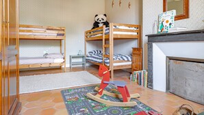 Une chambre d’enfant avec des lits superposés, un cheval à bascule, une bibliothèque et une cheminée.