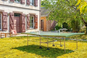 En tennisbane med et net, omgivet af græs og en bygning med røde skodder.