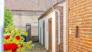 Une cour avec un mur en briques, un portail en métal et un bâtiment doté d’une porte blanche.
