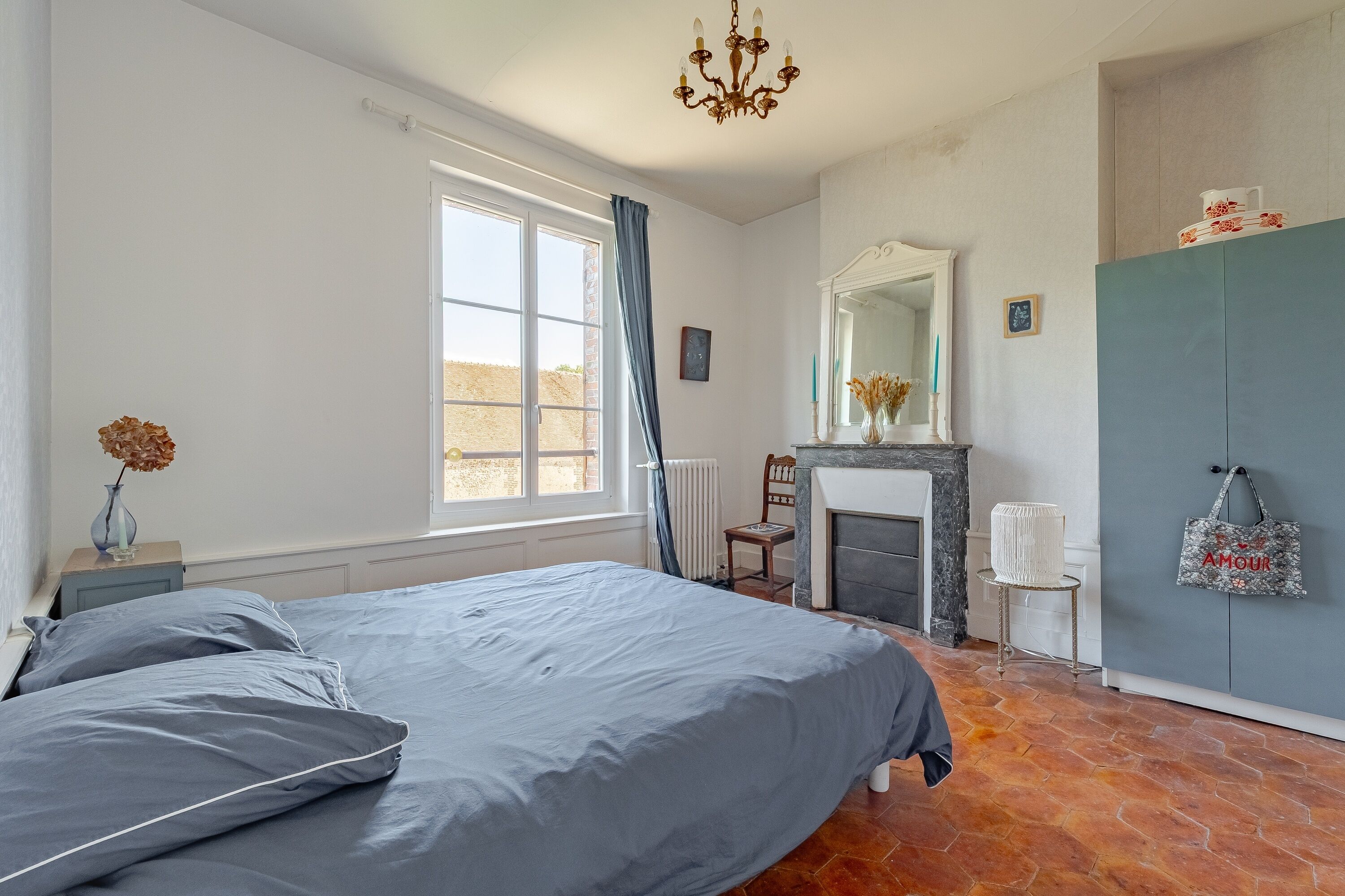 A bedroom with a bed, a dresser, a mirror, a fireplace, and a window.