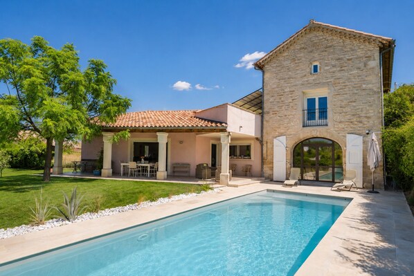 Una casa de dos pisos con piscina, mobiliario exterior y fachada de piedra.