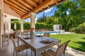 Un espacio de comedor al aire libre cubierto, con una piscina al fondo.