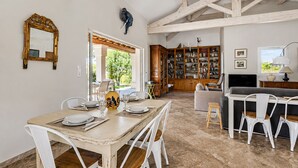 A dining area with a wooden table and chairs, a bookshelf filled with books, and a television in the background. - La Maison Rose - Avec Piscine Privée (Barjac)