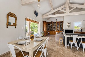 A dining area with a wooden table and chairs, a bookshelf filled with books, and a television in the background. - La Maison Rose - Avec Piscine Privée (Barjac)