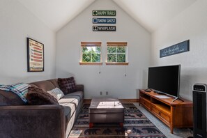 A living room with a couch, ottoman, TV, and a wall-mounted sign. - Serenity at Dover Bay | Sleeps 8 (Sandpoint)