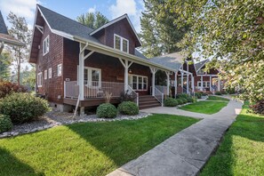 A two-story house with a porch, a front yard with a pathway, and a small garden area. - Serenity at Dover Bay | Sleeps 8 (Sandpoint)