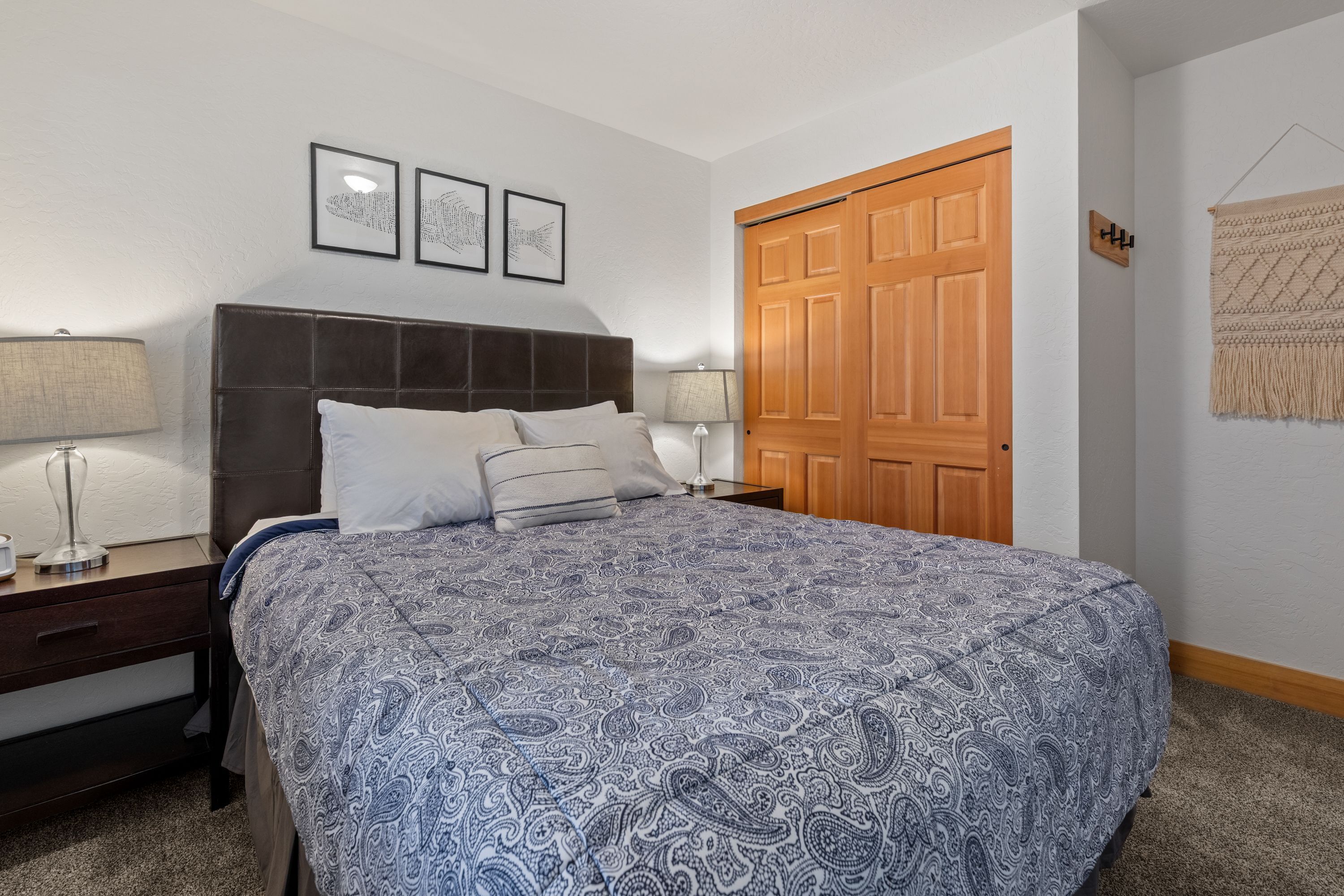 Une chambre à coucher avec un grand lit, deux tables de chevet avec des lampes, une porte en bois et une tapisserie accrochée au mur.