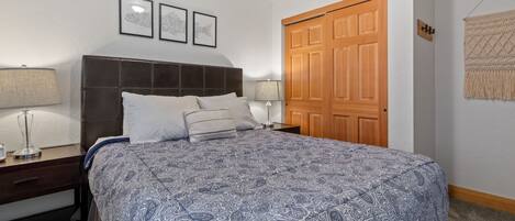 A bedroom with a large bed, two bedside tables with lamps, a wooden door, and a wall-mounted tapestry.