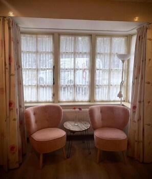 Una habitación con dos sillas rosadas, una mesita y un ventanal con cortinas.