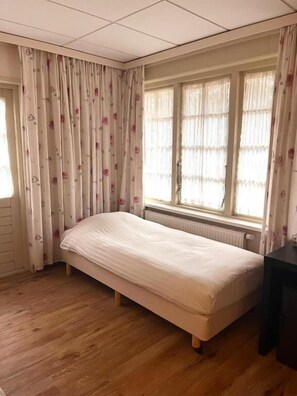 Una habitación con una cama individual, un radiador y un ventanal con cortinas.