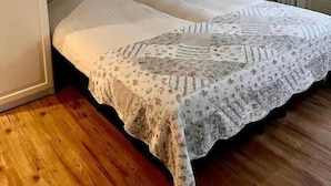 Un dormitorio con cama doble, armario, mesita y ventana con cortinas.