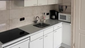 Una cocina moderna con armarios blancos, encimera negra, campana extractora de acero inoxidable, microondas y cafetera.