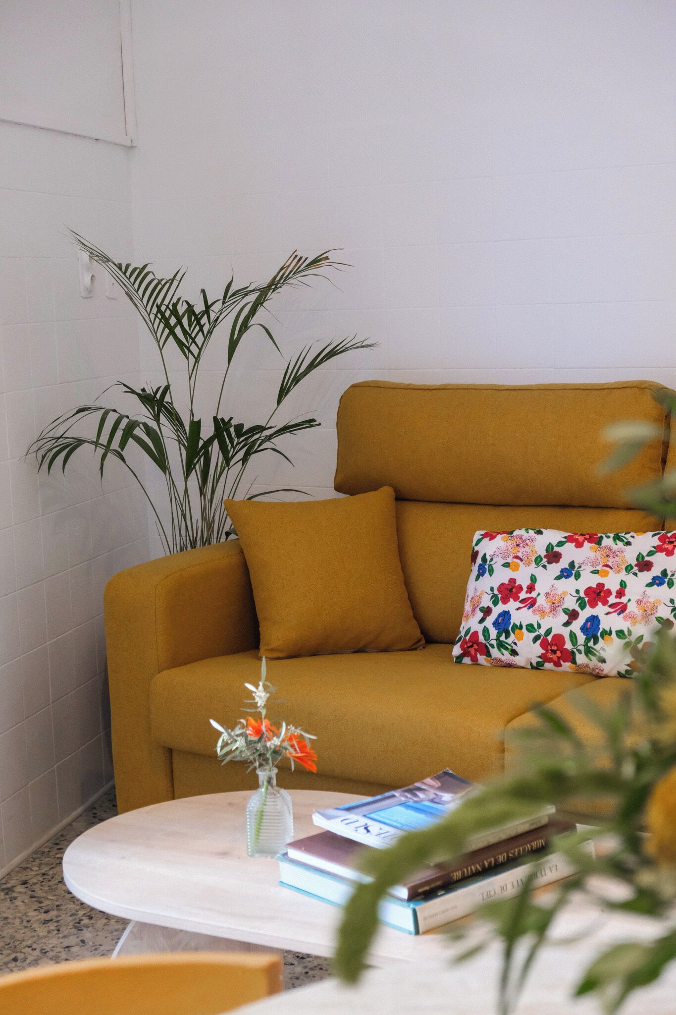 Een woonkamer met een bank, een bijzettafeltje, een plant en een bloemenkussen.