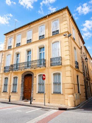 A multi-story building with a symmetrical facade, large windows, and a central entrance with a wooden door. - Maison Sarava – Superior Apartment with Separate Studio & Private Patio (Espira-de-l'Agly)