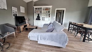 A modern living room with a sofa, a television, a dining table with chairs, and a cabinet with various items. - Villa on the outskirts of Geneva, between the lake and the mountains (Douvaine)