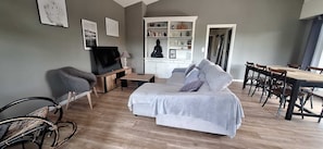 Ein modernes Wohnzimmer mit einer Couch, einem Fernseher, einem Esstisch mit Stühlen und einer Kommode mit diversen Gegenständen.