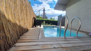 A swimming pool with a wooden deck and metal ladders, surrounded by a bamboo fence and a house. - Villa on the outskirts of Geneva, between the lake and the mountains (Douvaine)