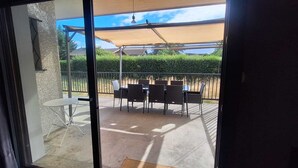 A view through a glass door onto an outdoor patio with a table and chairs, a pergola, and a hedge. - Villa on the outskirts of Geneva, between the lake and the mountains (Douvaine)